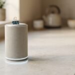 Small cylindrical smart speaker with a glowing base light ring on a kitchen counter, illustrating the Google Home Speaker
